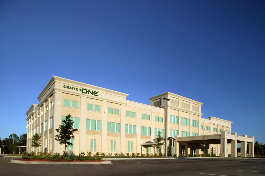 A four-story building displays the "CenterOne" sign in green letters. It serves as a state-of-the-art Medical Office Building, with a manicured lawn gracing the foreground.