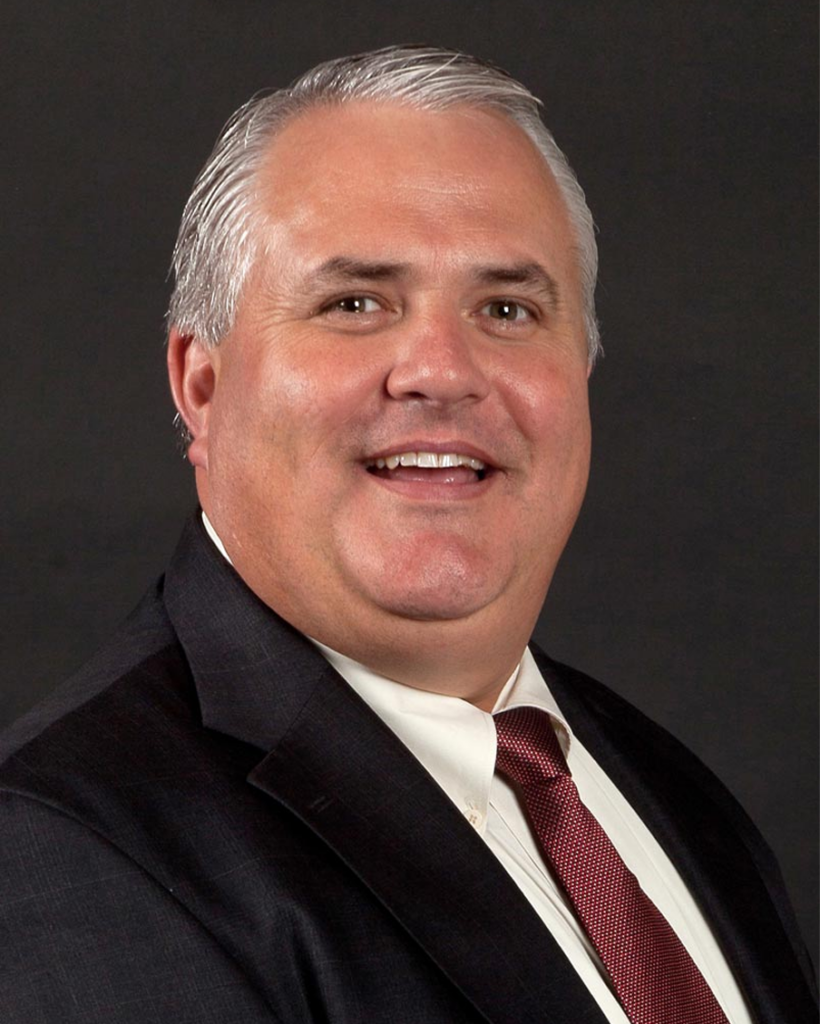 A smiling man in a suit and tie poses against a dark background.