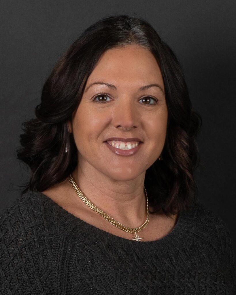 Courtney Johnson, a woman with shoulder-length dark hair and a gray sweater, smiles warmly against a dark background.