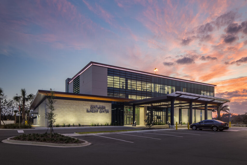 Centurion Surgery Center surrounded by an orange-tinged sky and lighted parking lot.