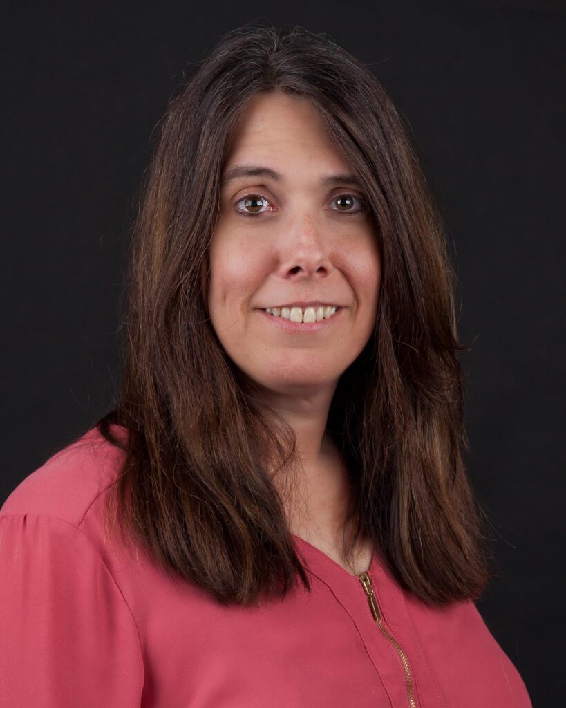 Rosemarie Palmer, a woman with long brown hair, beams in a pink top against a black background.