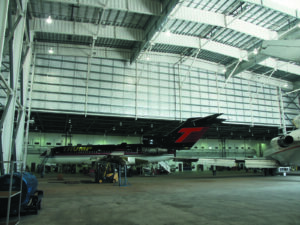 A black private jet with "TRUMP" written on its side is parked inside the spacious, well-lit Flightstar Hanger, showcasing recent tenant improvements and expansion.