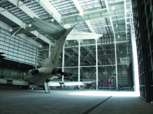 A large jet aircraft is parked inside the spacious, well-lit Flightstar maintenance hangar with high ceilings and open doors, showcasing recent Tenant Improvements from the Hanger 815 Expansion.