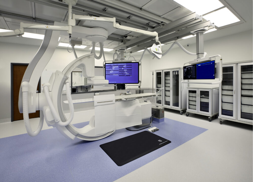 A modern Ambulatory Surgery Center operating room at First Coast Cardiovascular Institute (FCCI), featuring advanced medical imaging equipment, monitors, storage cabinets, and a clean, organized environment.
